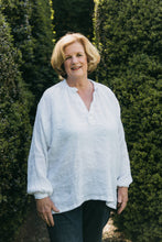 Load image into Gallery viewer, Older woman wearing French Cheesemaker's Smock made from white linen, standing by a large hedge