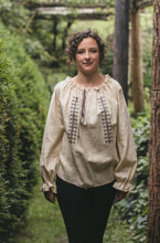 Load image into Gallery viewer, Young woman walking towards camera outdoors with greenery surrounding her. She is wearing 103 Romanian Blouse. Blouse is natural linen with traditional embroidery. Paired with plain black pants.