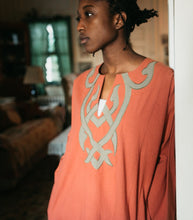 Load image into Gallery viewer, Close up photo of model in coral colored Egyptian Shirt. Shows details of gray applique on front.