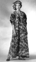 Load image into Gallery viewer, Woman wearing 105 Syrian Dress. Dress is ankle length and sleeves are pushed up to below elbow. fabric is an abstract geometric print. Model has a scarf tied around head and is photographed with a white background.