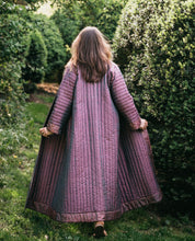 Load image into Gallery viewer, Back view of model walking away from camera outdoors wearing lavender silk Turkish coat. Coat has full trapunto quilting and is ankle length. Model is holding jacket out at hip level showing full width.