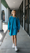 Load image into Gallery viewer, Photo of young girl wearing a blue corduroy Smock. Model is walking outside on sidewalk in front of stores.