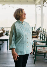 Load image into Gallery viewer, Older white woman smiling standing on the porch facing to the right, wearing Chinese pajama jacket in light teal..
