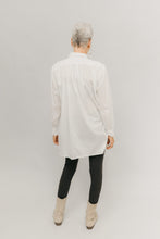 Load image into Gallery viewer, Woman standing in front of light grey background wearing a white Croatian shirt as a tunic with black leggings and boots. Her back is facing.