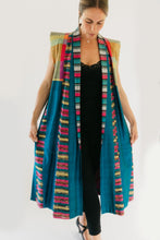 Load image into Gallery viewer, Woman wearing multi colored 118 Tibetan Panel coat. Standing in front of white background holding sides out in hands. coat is primarially blue with multicolored shoulders and trim.