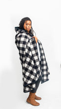 Load image into Gallery viewer, Black woman standing sideways wearing a large black and white checked burnoose with brown boots