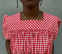 Load image into Gallery viewer, Close up of the bodice of Woman standing in front of grey wall wearing a red and white check dress with short puffed sleeves and a bottom flounce.