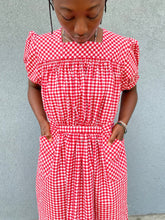 Load image into Gallery viewer, Close up of woman standing in front of grey wall wearing a red and white check dress with short puffed sleeves and a bottom flounce.