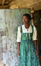 Load image into Gallery viewer, Young woman wearing green Dirndel (View B dress with View A Blouse). She is standing in front of a wood door. Model is looking over her right shoulder with her hands by her sides.