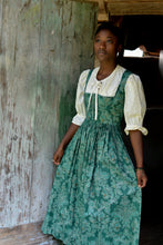Load image into Gallery viewer, Young woman wearing green Dirndl (View B dress with View A Blouse). She is standing in front of a wood door holding skirt in both hands by her side.