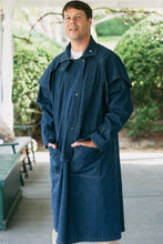 Load image into Gallery viewer, Man standing on a porch wearing a dark blue Drover's Coat. hands in pockets.