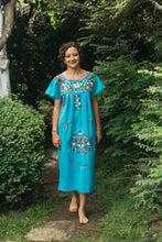 Load image into Gallery viewer, Photo of a young woman walking barefoot outdoors wearing a blue Old Mexico dress with colorful floral embroidery.