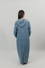 Load image into Gallery viewer, Asian woman wearing a floor length blue and white vertical striped Djellaba with her hands in her pockets. Back view. Background is white back drop.