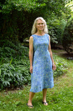 Load image into Gallery viewer, White woman wearing a sleeveless blue batiked muumuu, standing outside by shrubery.