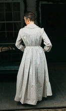 Load image into Gallery viewer, Photo of back view of prairie dress and apron waistband. Model stands outside with hands in front pocket.