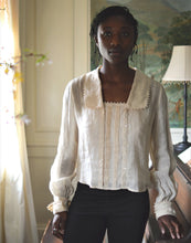 Load image into Gallery viewer, African woman standing in a room beside a piano wearing 210 Armistice Blouse and black leggings.