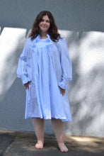 Load image into Gallery viewer, Young woman standing in front of a grey wall in a light blue ruffled nightgown.