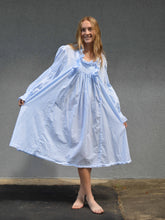 Load image into Gallery viewer, Young woman standing in front of a grey wall in a light blue ruffled nightgown.