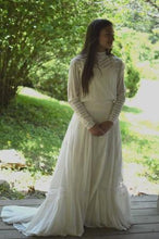 Load image into Gallery viewer, Young brunette woman standing on a wooden platform surrounded by greenery, wearing 227 Edwardian Bridal Gown and Dress.