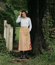 Load image into Gallery viewer, Woman standing in front of an open gate surrounded by greenery wearing the 231 Big Sky Riding Skirt buttoned to the left for a skirt effect.