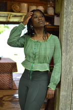 Load image into Gallery viewer, Front of African American woman leaning on a door frame with right hand moving her hair wearing a green check 234 long sleeved version camisole and dark green athletic leggings.