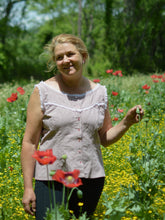 Load image into Gallery viewer, smiling middle aged white, blonde woman standing with left hand on a poppy bud wearing sleeveless camisole in pale pink with white ruffle lace and black athletic leggings she is standing in a field of red poppies.