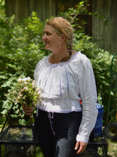 Load image into Gallery viewer, smiling middle aged white woman wearing a long sleeved camisole in white with white lace and black leggings with greenery in the background holding a bouquet.