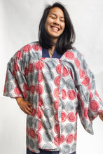 Load image into Gallery viewer, Smiling woman wearing a red and grey spiral printed ankara fabric made into a Michiyuki over a blue cotton kimono. In front of a white back drop.