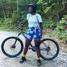 Load image into Gallery viewer, Person standing with a bicycle on a trail in a forest wearing blue floral biking shorts.