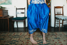 Load image into Gallery viewer, Person wearing blue harem pants from the Algerian Suit with white patterns in a room with chairs and a rug.