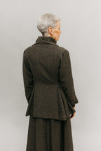 Load image into Gallery viewer, Older white woman standing in font of a white studio backdrop, wearing the traveling suit back facing the audience showing the flared below the hip peplum and the high stand collar