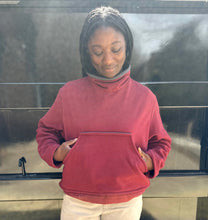 Load image into Gallery viewer, Woman in red mock sweater standing in front of black wall