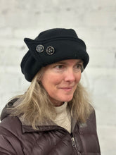 Load image into Gallery viewer, Woman wearing a black roll brim hat with two buttons on it, looking slightly away from the camera