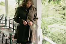 Load image into Gallery viewer, Brunette White woman standing on a porch with greenery in the background buttoning the Countryside Frock Coat.