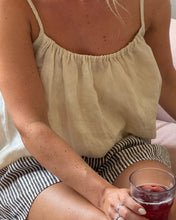 Load image into Gallery viewer, Person wearing a light-colored top and striped shorts, holding a glass of red wine.