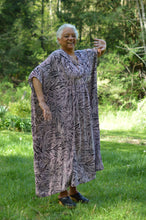 Load image into Gallery viewer, Dancing older African American woman wearing Kaftan in a black and pink stripe like print with greenery in the background.