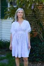 Load image into Gallery viewer, white woman wearing a knee length Kaftan in a lilac and white stripe fabric standing in front of a house with greenery.