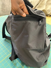 Load image into Gallery viewer, Gray backpack with a zipper held by a hand on a green cutting mat.