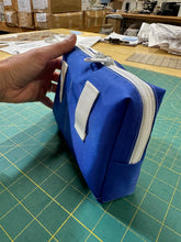 Load image into Gallery viewer, Blue pouch with a white zipper held by a hand on a green cutting mat.