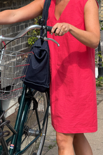 Load image into Gallery viewer, Woman in a red dress holding a navy bag next to a bicycle on a sidewalk.