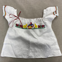 Load image into Gallery viewer, Flat lay of the Mexican Baby Dress in white linen with red, blue, yellow, and green embroidery on the yoke and sleeves.