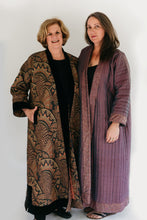 Load image into Gallery viewer, Photograph of two women standing side by side.  Woman on the left is wearing a tapestry fabric Turkish coat with trapunto trim around sleeves, front opening and bottom hem. Woman on right is wearing a solid lavandar silk coat with trapunto stitching all over the body of coat.
