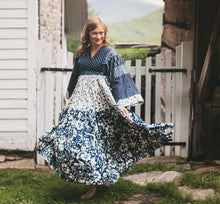 Load image into Gallery viewer, Woman walking towards camera in mulit fabric blue floral Afghan Nomad Dress.  Skirt is swishing as she walks.  White gate is behind her with a mountain view in distance
