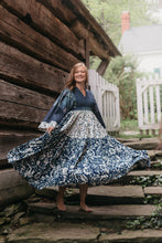 Load image into Gallery viewer, Woman twirling with full skirt in mid air.  Dress is multi fabrics all are various blue and white floral prints.  Woman is on stone stairs outdoors with wooden building behind her.

