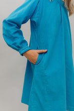 Load image into Gallery viewer, Photo of young girl wearing a blue corduroy Smock. Photo shows close up of sleeve cuff and side seam. Girl has her hand in the pocket at side.

