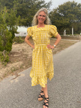 Load image into Gallery viewer, Woman wearing a yellow and white checked calf-length dress with puffed sleeves and pockets.  Standing outside in a street, wearing black strapped sandals.
