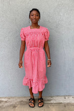 Load image into Gallery viewer, Woman standing in front of grey wall wearing a red and white check dress with short puffed sleeves and a bottom flounce.
