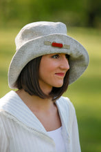 Load image into Gallery viewer, Young brunette white woman wearing a white blouse and the side view of the Metropolitan Hat in gray with a red brooch on the brim
