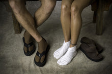 Load image into Gallery viewer, Photo of Tabi socks on seated man and woman. Man is on left and wears tabi socks with flip flop sandals. Woman wears just socks and has flip flops next to her left side.
