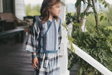 Load image into Gallery viewer, Young girl in a plaid kimono and vest standing on a porch with greenery in the background
